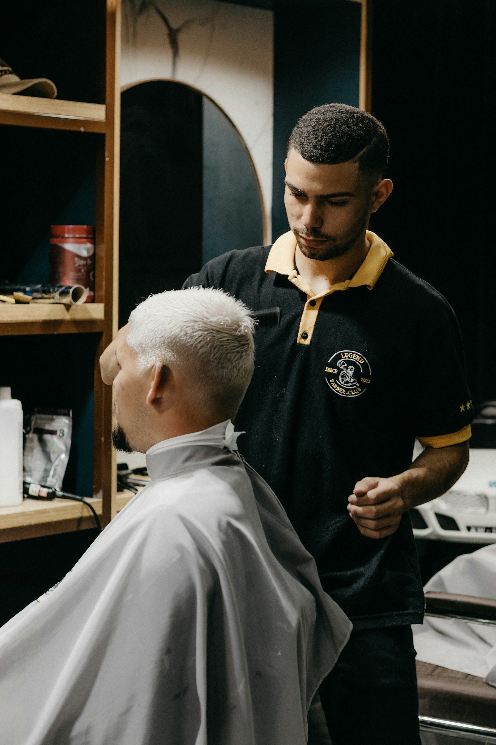 Emre Kaya steht im Barbershop hinter seinem Kunden und prüft die Kontur am kurz geschnittenen Haar
