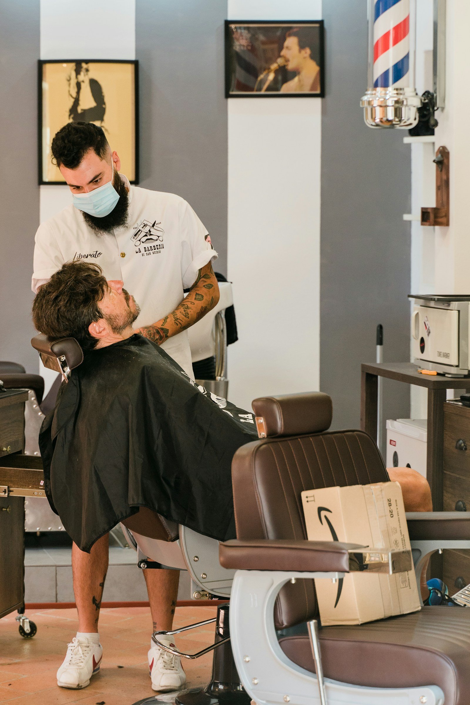 Luca Hoffmann arbeitet an einem zurückgelehnten Kunden im Barberstuhl, im Hintergrund eine Barbierstange