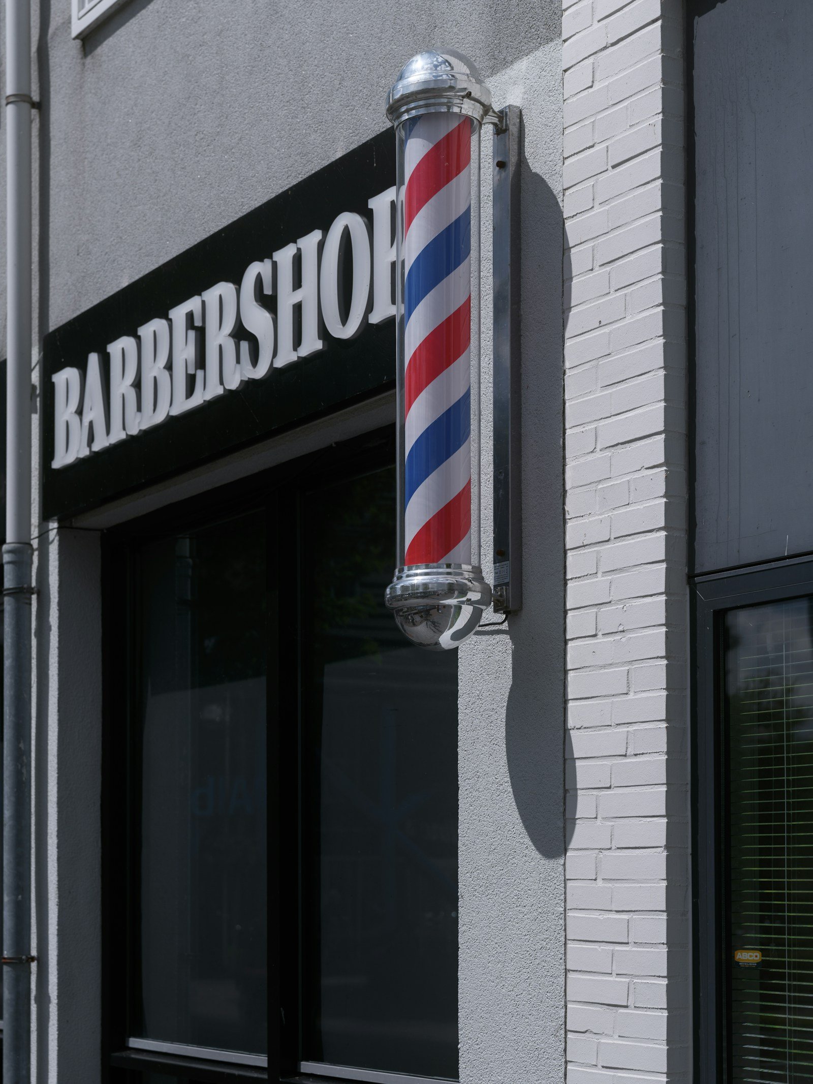 Ladenfront von KLINGE: Barbierstange neben dem Schild „Barbershop“ über der Eingangstür